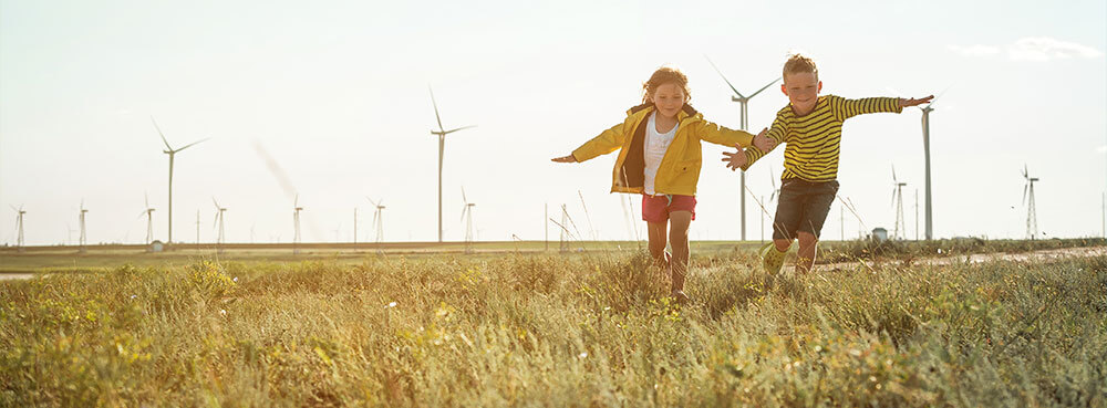 2 children running in a field with wind turbines - sustainability